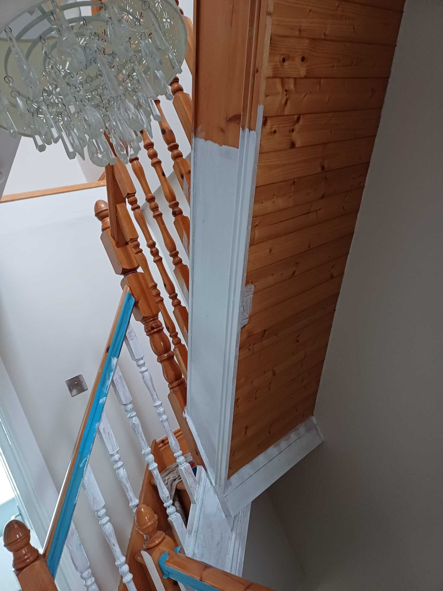 a staircase that is dark oak colour with a glass chandelier. The hallway has been partially painted white.